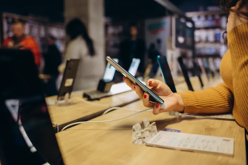 Shopper holding a phone at a retail display table of smartphones